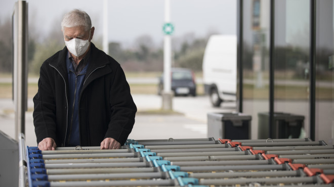 Mann mit Atemschutzmaske räumt Einkaufswagen ein
