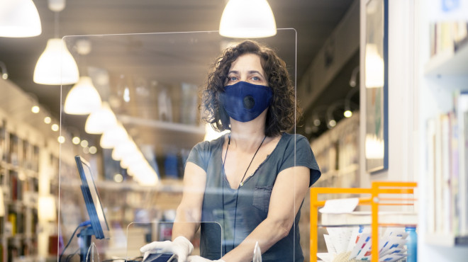 Verkäuferin mit Mundschutz hinter einer Plexiglasscheibe