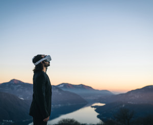 Person mit Virtual Reality Brille schaut ins Weite Hintergrund See und Gebirge