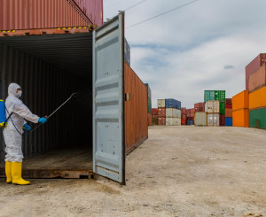Mann in Schutzanzug desinfiziert einen Gütercontainer