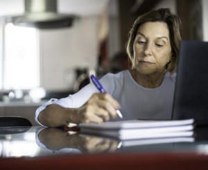 Frau mittleren Alters macht Notizen neben dem Computer