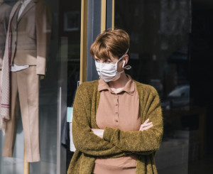 Frau mit Maske steht vor ihrem geschlossenen Kleidergeschäft