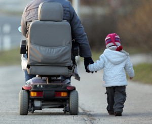 Person in Rollstuhl mit Kind an der Hand